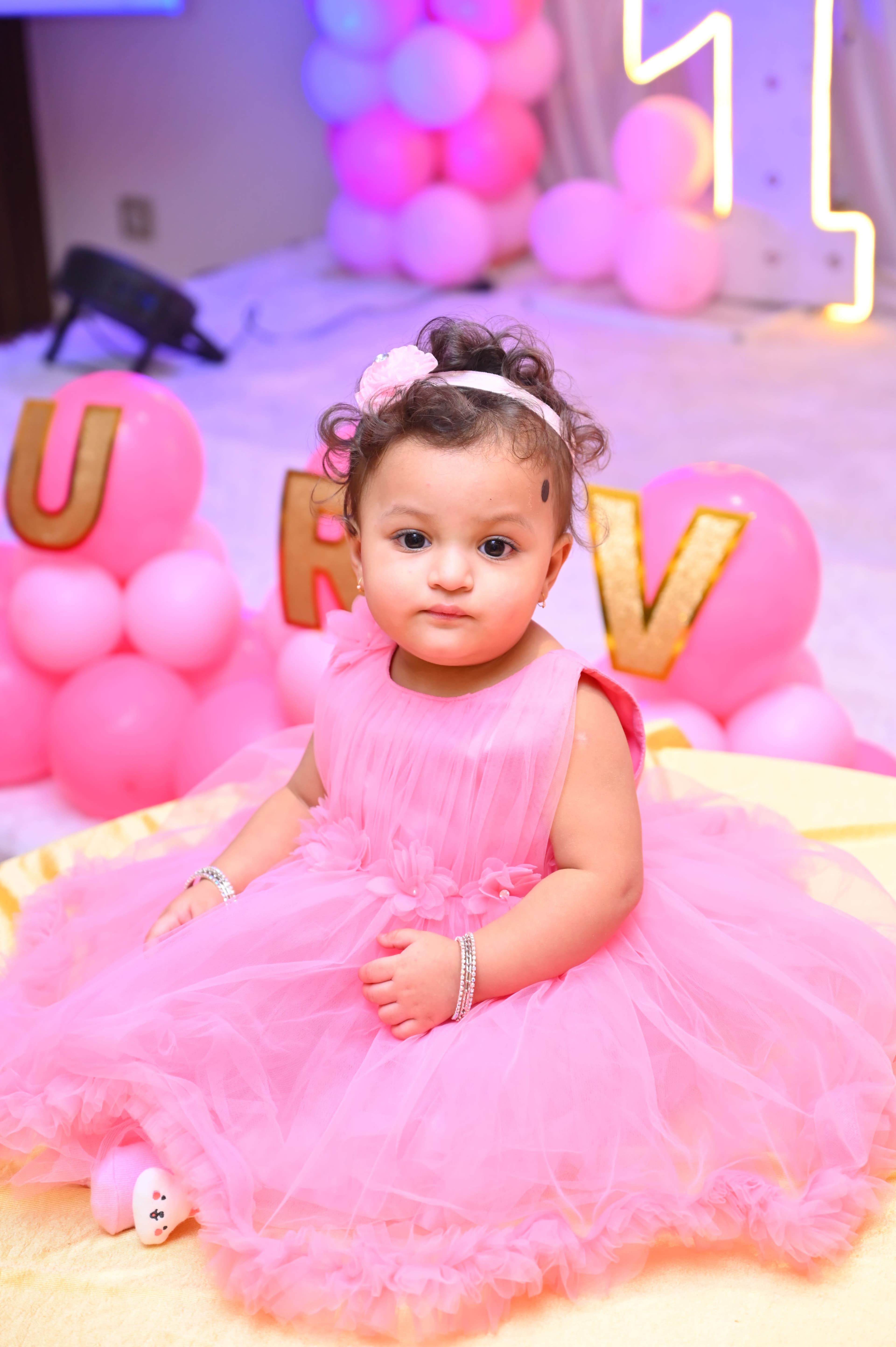 Baby girl in a pink party dress in front of balloon letters
