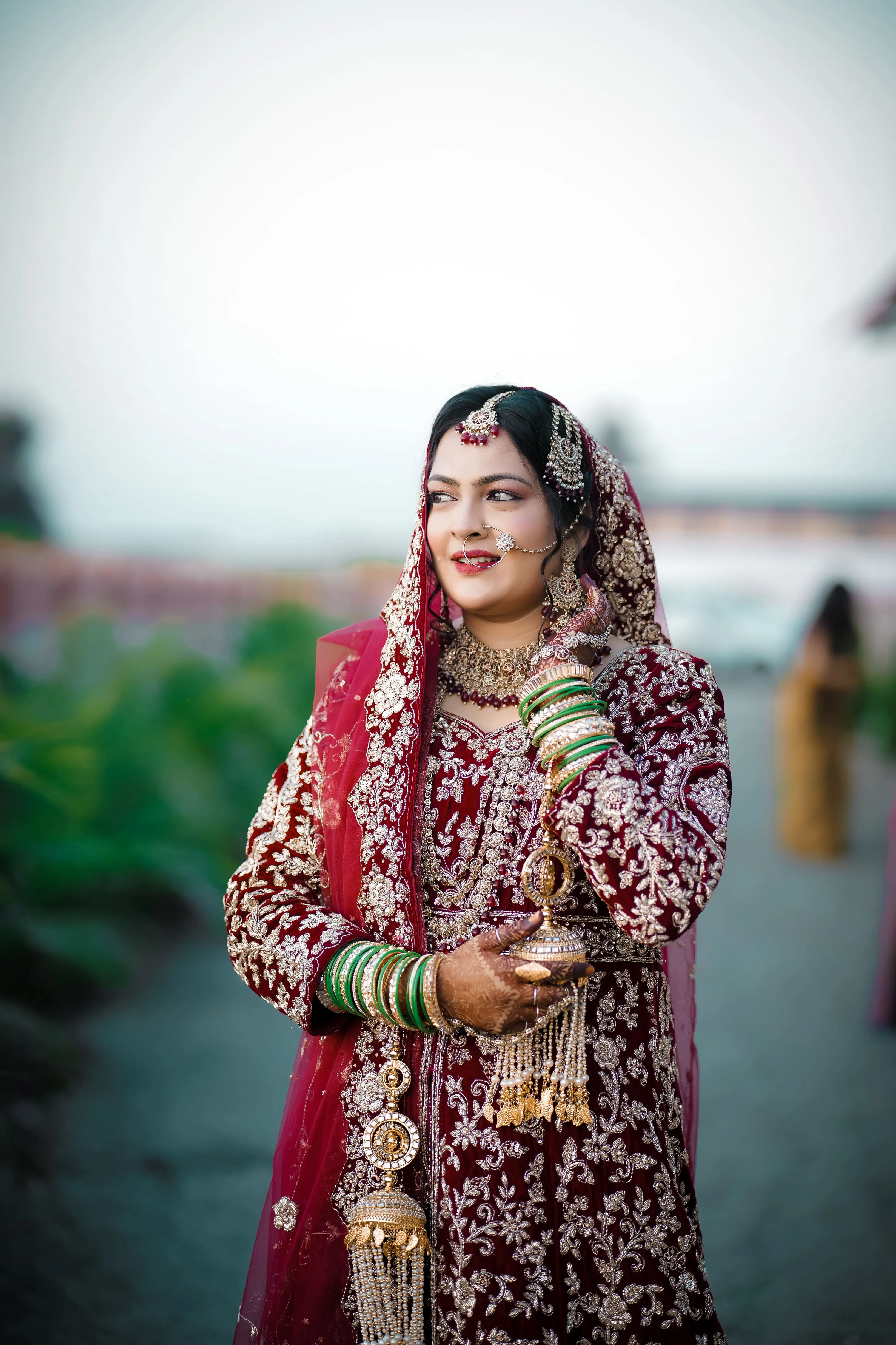 Bride in a maroon embroidered lehenga and bridal jewellery, outdoor portrait
